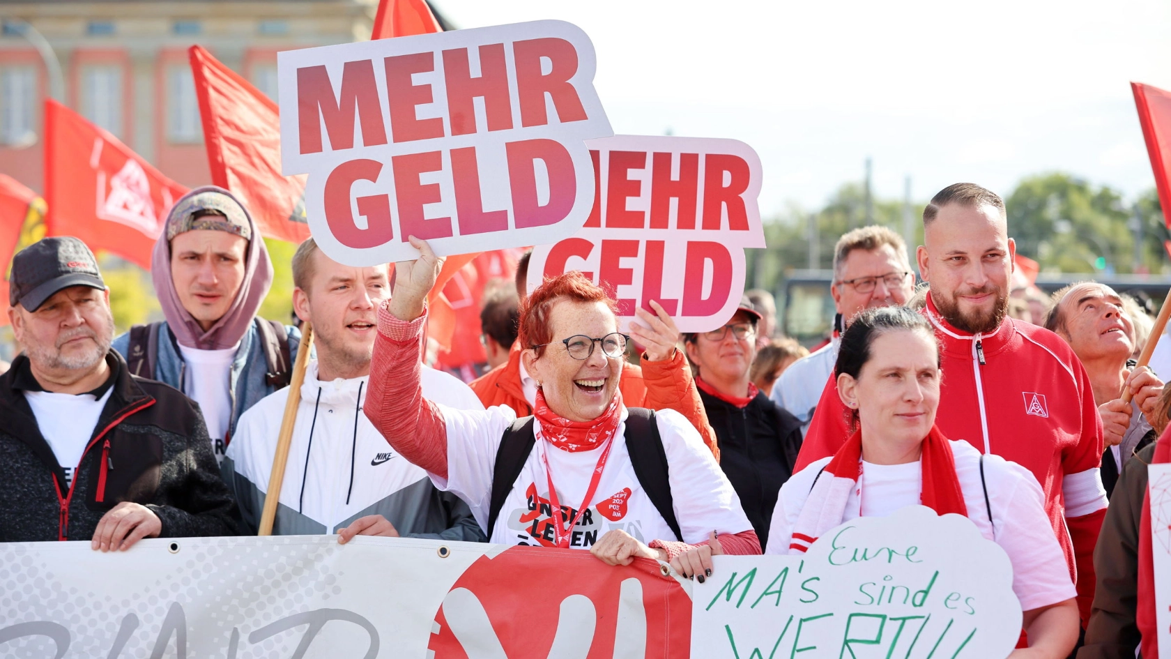 Beim Tarifauftakt in Potsdam hält eine Frau in der Menschenmenge ein Schild hoch „Mehr Geld“.