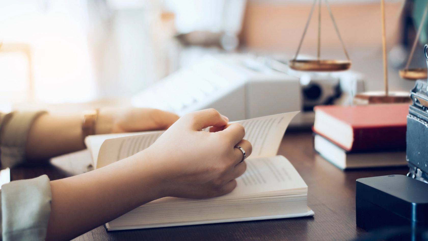 Eine Anwältin liest Gesetzbücher im Büro, im Hintergrund sind Bücher und eine Richterwaage zu sehen