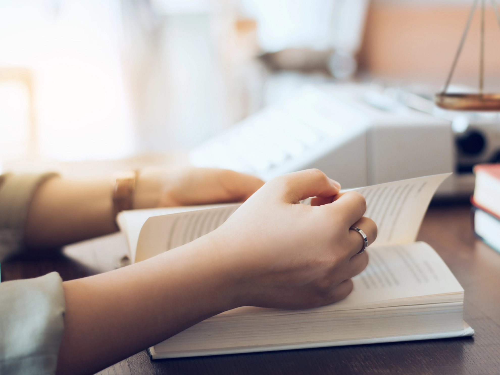 Eine Anwältin liest Gesetzbücher im Büro, im Hintergrund sind Bücher und eine Richterwaage zu sehen
